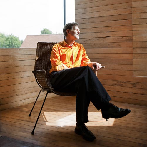 John Christophers, architect of zero carbon house, Birmingham sits in the studio in an orange shirt