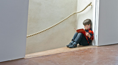 Theo reads a book sitting at the top of the stairs in zero carbon house, Birmingham with the hemp stair rail also in view